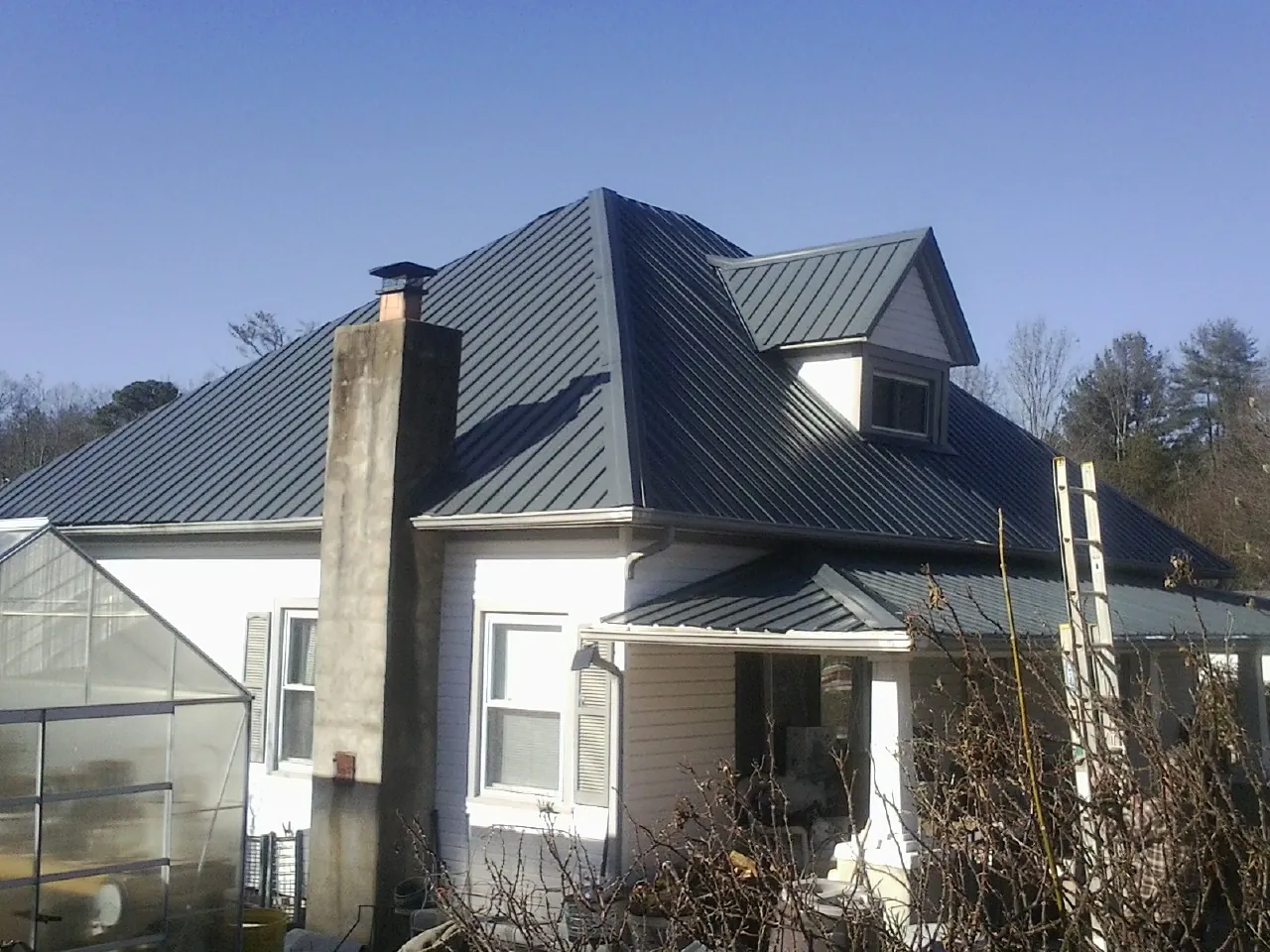 Dark blue standing seam metal roof on a white farmhouse with dormer — Slate & Tile Roof Repair by Roofing Brothers in Longmont
