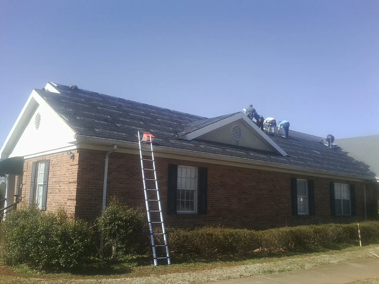Crew tearing shingles off a brick ranch roof with a ladder set — Emergency Roof Repair work by our crew in Longmont