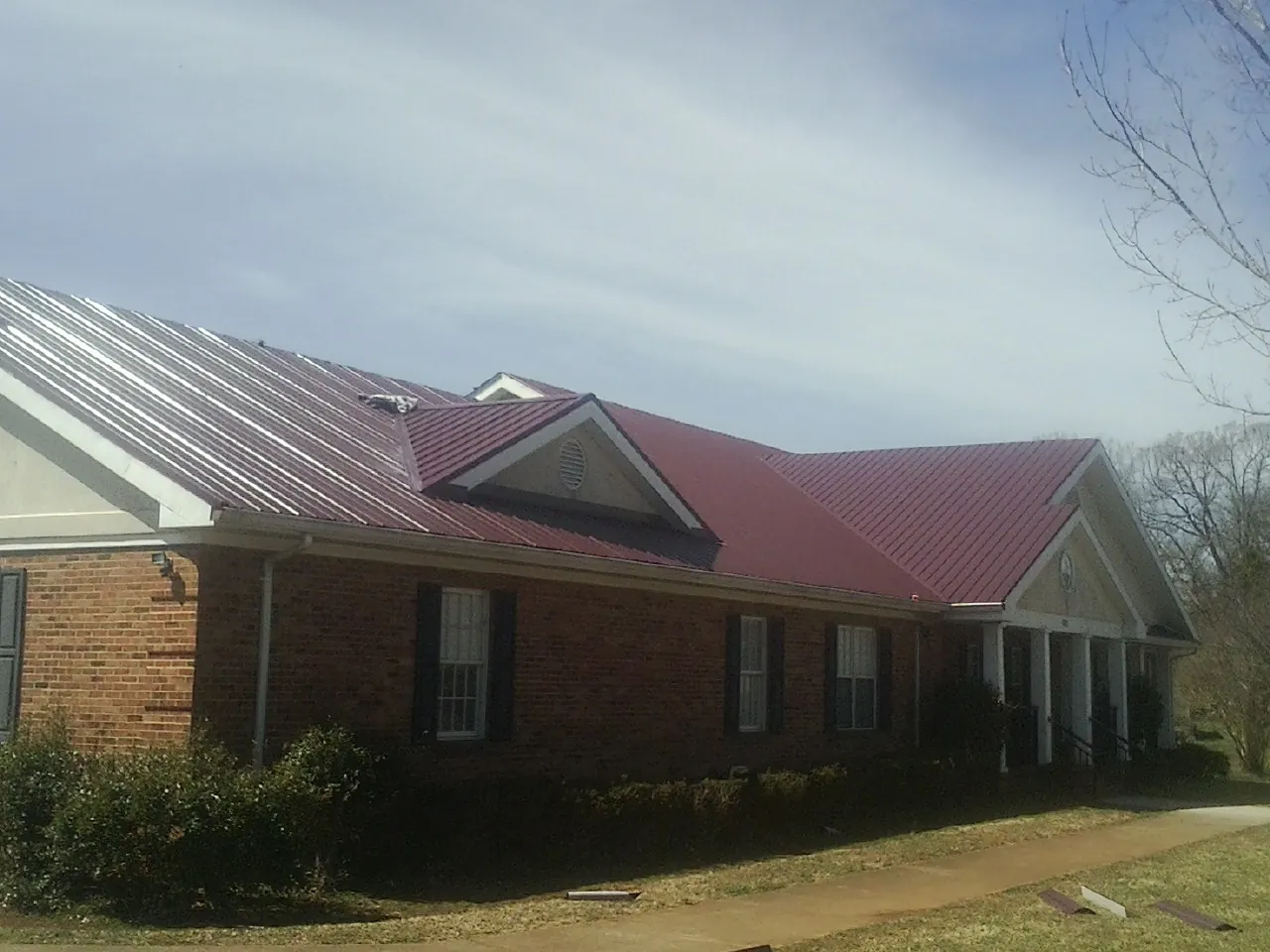 Red metal roof with gabled entries on a long brick building, from a Hail Damage Roof Repair job in Longmont