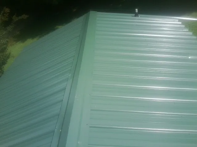 New green metal panels meeting at the ridge of a roof — Flat Roof Repair work by our crew in Longmont
