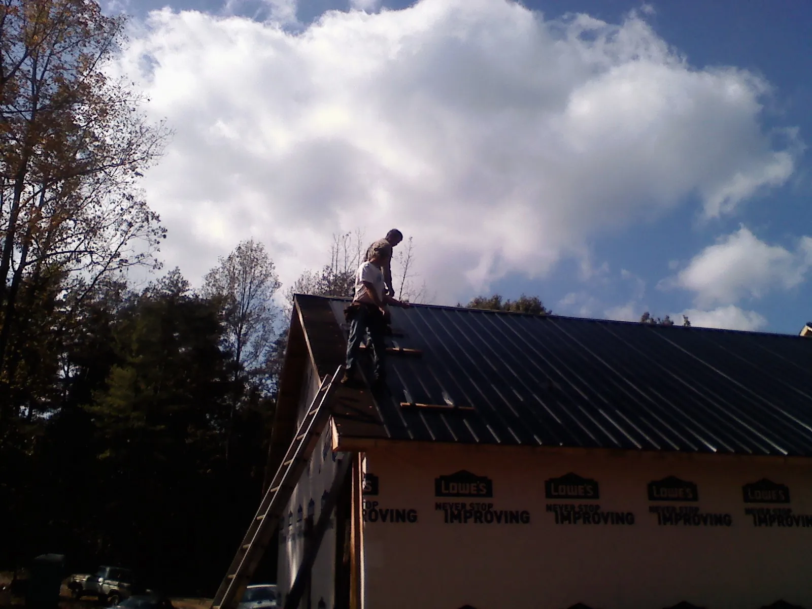 Roofer fastening dark metal panels high against a cloudy sky, from a Roof Inspection job in Longmont